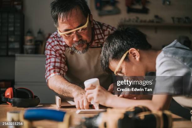 asiatique chinois charpentier senior enseignant le travail du bois à son petit-fils dans un atelier de menuiserie - retraités qui travaillent photos et images de collection