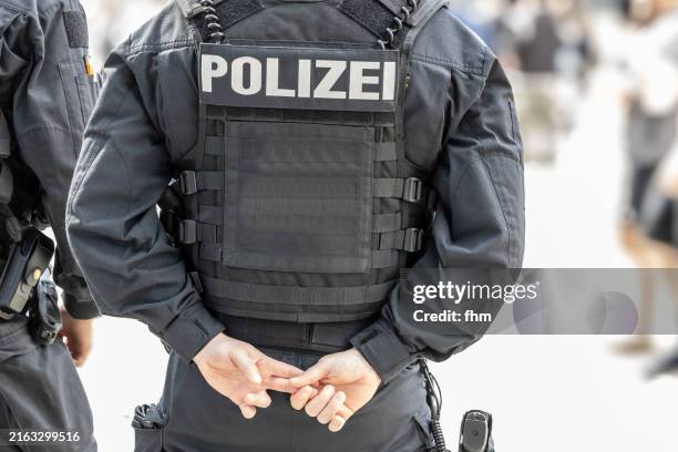 german police officer with bulletproof vest and gun observes relaxed the town - kugelsicher stock-fotos und bilder