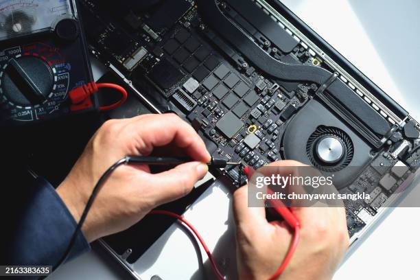 computer technician A laptop motherboard repairman is using an IC meter to find defects on the motherboard to repair on his table.