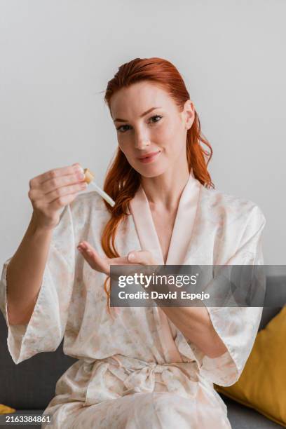 beautiful redhead woman applying serum on her face for skincare routine - schoonheidsspecialist natuur stockfoto's en -beelden