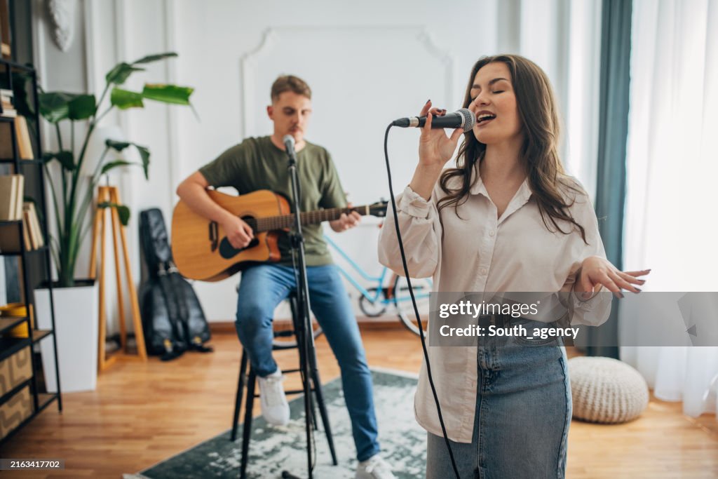 Duo performing with guitar and microphone indoors, smiling