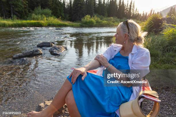 mujer madura se relaja en silla en la orilla del río - pies cruzados en los tobillos fotografías e imágenes de stock