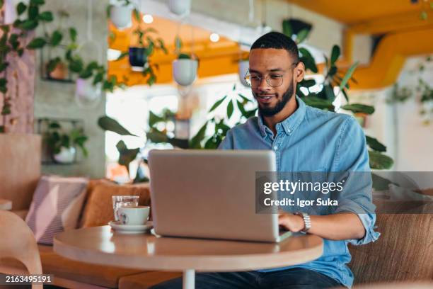 young man sitting in coffee shop and using laptop - usar portátil imagens e fotografias de stock