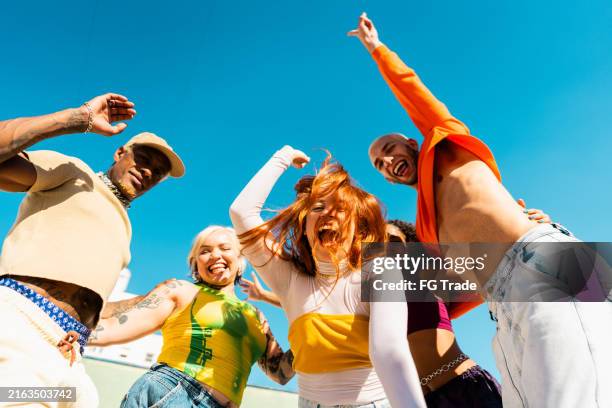 portrait of lgbtqia+ friends jumping at rooftop - arme hoch stock-fotos und bilder