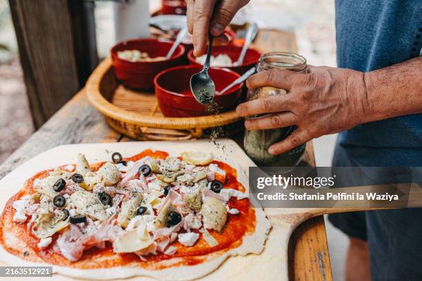 hand adding oregano on pizza - origano foto e immagini stock