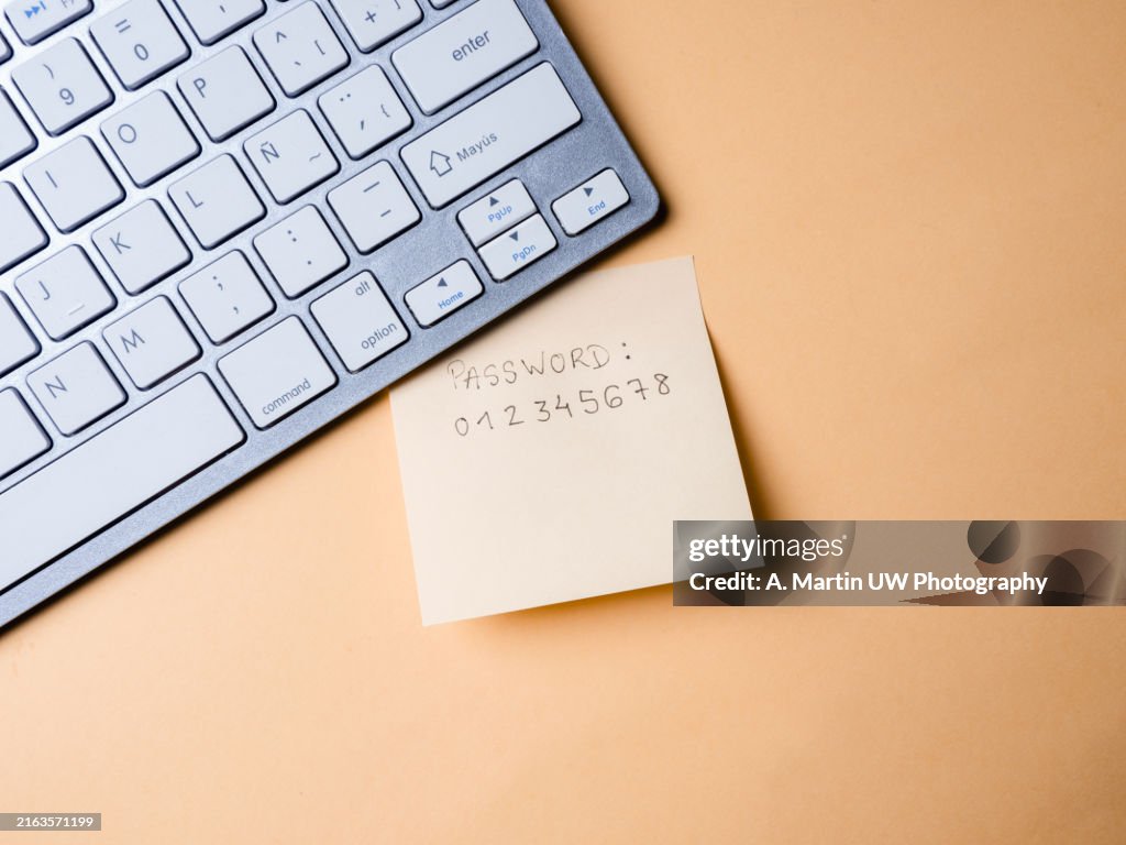 Top down view of yellow adhesive note with unsafe password under computer keyboard on desk, security issues concept