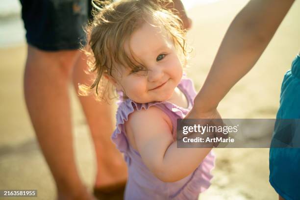 first steps of a happy little girl on the beach with support of her father and brother - flickbaby bildbanksfoton och bilder