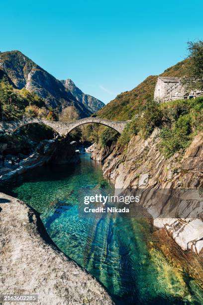 atemberaubende alte steinbrücke über den klaren fluss in der schweiz - valle verzasca stock-fotos und bilder