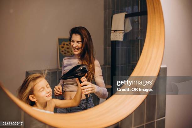 laughing mother blow-drying daughter's hair in bathroom at home - hair dryer stock pictures, royalty-free photos & images