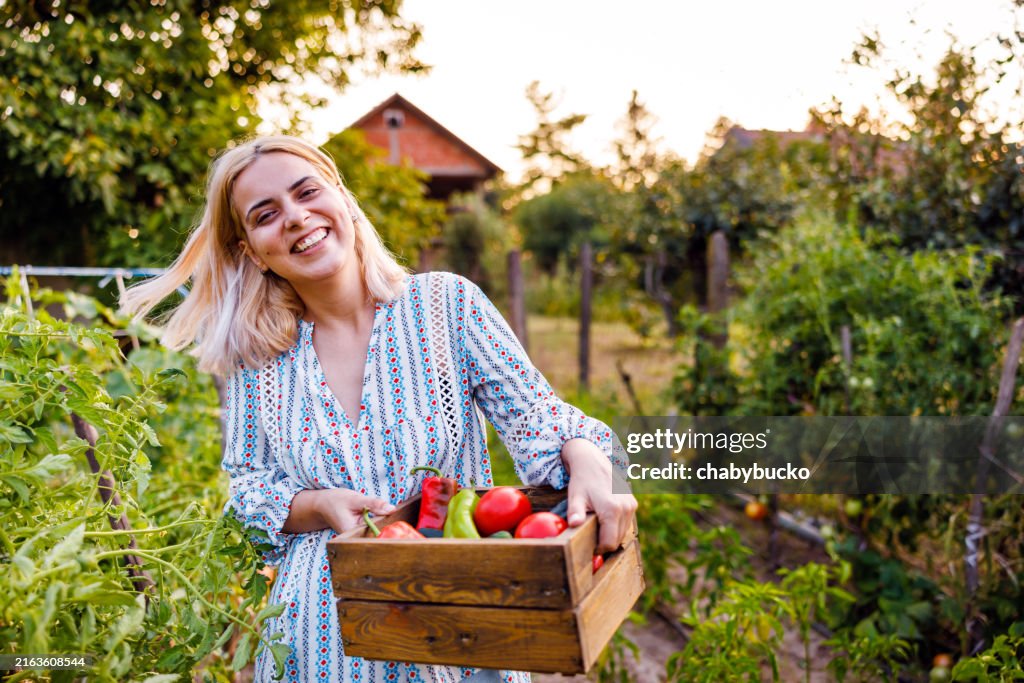 Glückliche Frau, die für die Kamera posiert, während sie frisches Gemüse im Korb trägt