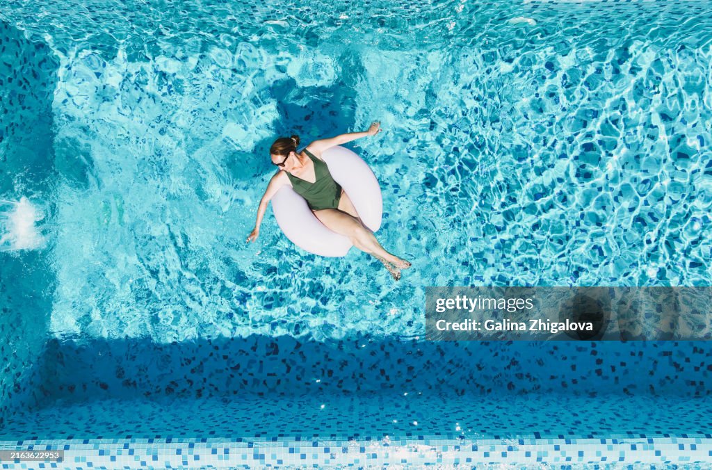 Adult smiling brunette woman enjoying life while swimming on inflatable ring in pool