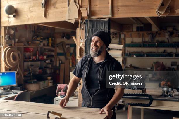 smiling carpenter standing at workbench in a workshop - menuiserie photos et images de collection