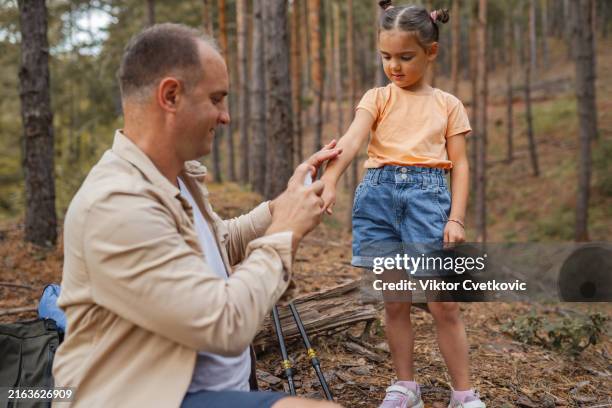 father spraying tick repellent on his little daughter's arm during hike in nature - morder imagens e fotografias de stock
