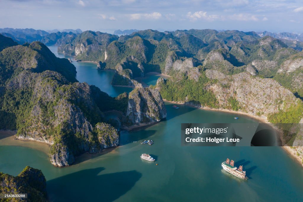 Aerial of boutique cruise ship Ylang (Heritage Line) with full sails in front of karst islands