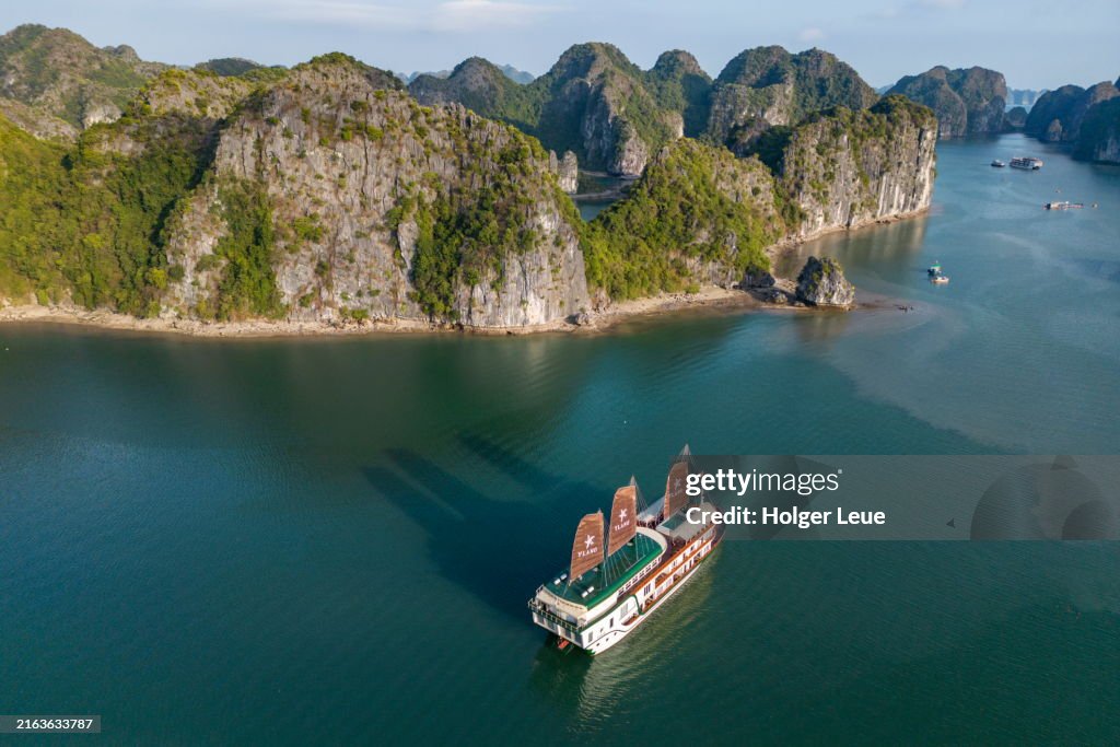 Aerial of boutique cruise ship Ylang (Heritage Line) with full sails in bay amidst karst islands