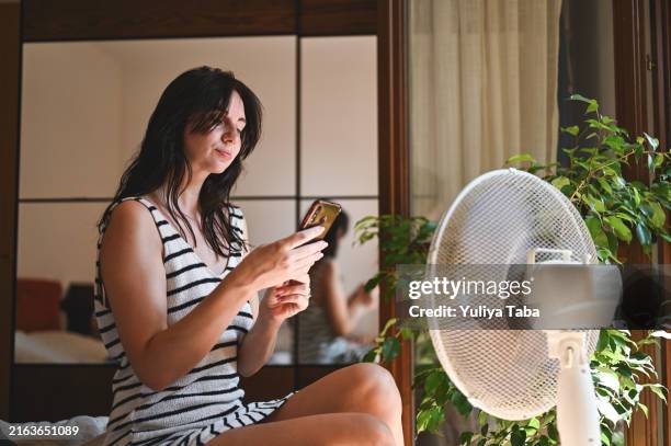 mid adult woman with mobile phone in front of fan. - hand fan stock pictures, royalty-free photos & images