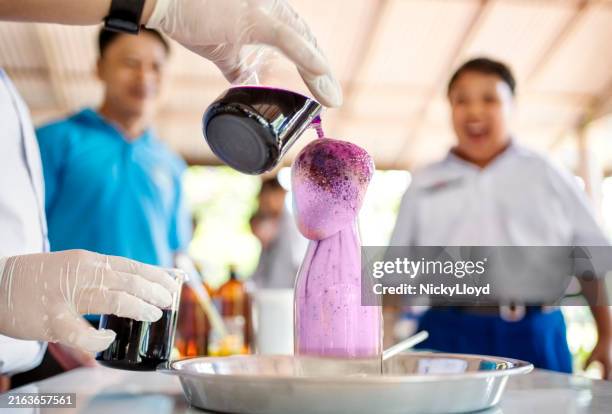 studente che fa un esperimento scientifico in laboratorio con insegnante e compagno di classe che guardano - reazione chimica foto e immagini stock