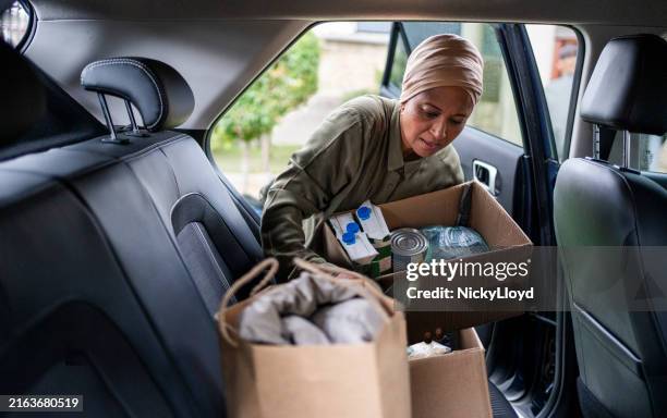 muslim woman putting boxes into her car to deliver to a charity - banco alimentar imagens e fotografias de stock