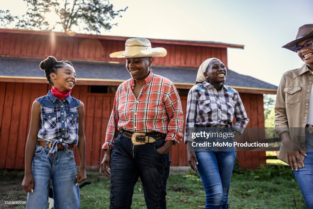 Multi-generational cowgirls walking in front of barn
