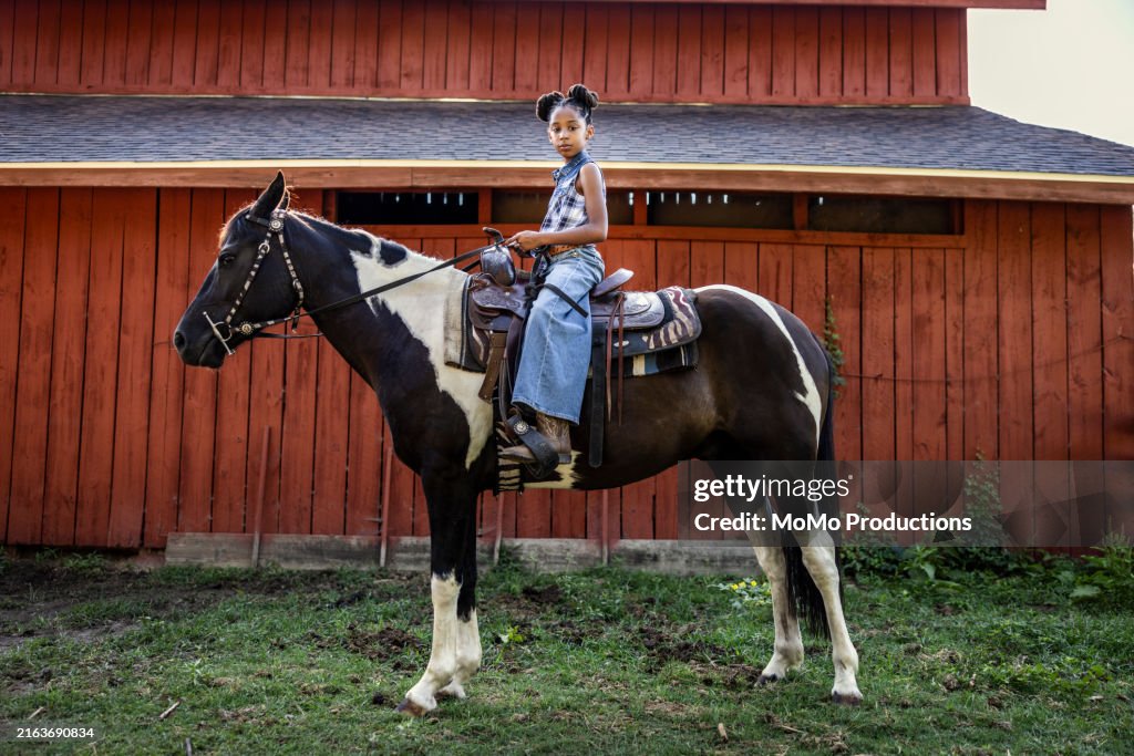 Portrait of young girl sitting on horse in front of barn