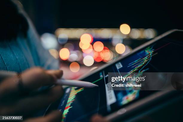 primer plano de manos femeninas sosteniendo un teléfono móvil, navegando por los gráficos del mercado de valores en una calle de la ciudad por la noche, con el coche borroso y las luces de la calle en el fondo - fiscal fotografías e imágenes de stock