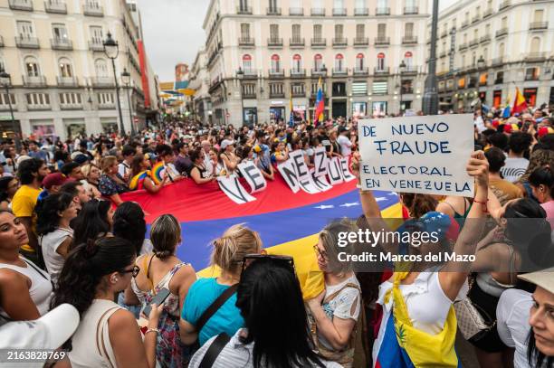 People hold a large Venezuelan flag during a demonstration. Venezuelans residing in Madrid gathered in Puerta del Sol to protest and express their...