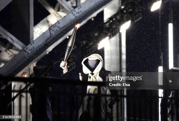 Torch bearer performs on the Debilly Footbridge during the opening ceremony of the Olympic Games Paris 2024 on July 26, 2024 in Paris, France.