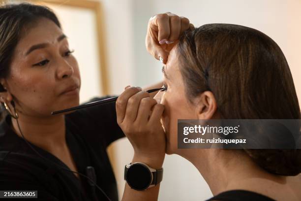 woman putting on makeup in a beauty salon for her daughter's graduation party - makeup artist stock pictures, royalty-free photos & images
