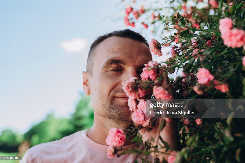 Young man enjoys the scent of pink roses in hand against a blue sky background.