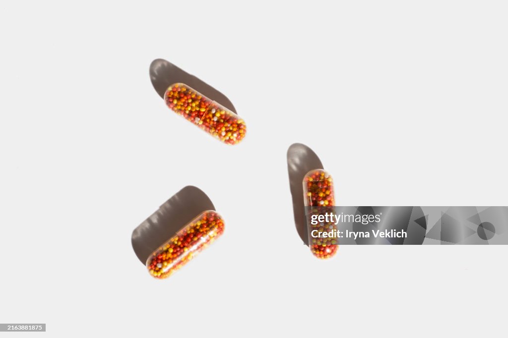 Transparent capsules with medicine in shape of colorful balls with iron, vitamin B, vitamin C, folic acid, zinc on a white background with shadow.