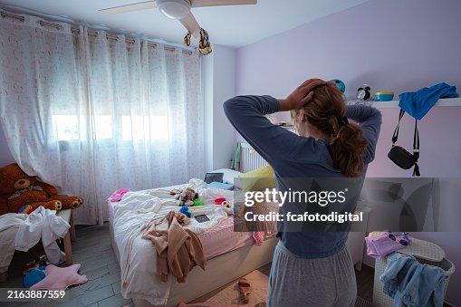 Teenager girl head in hands looking shocked her messy bedroom Teenager girl head in hands looking shocked her messy bedroom