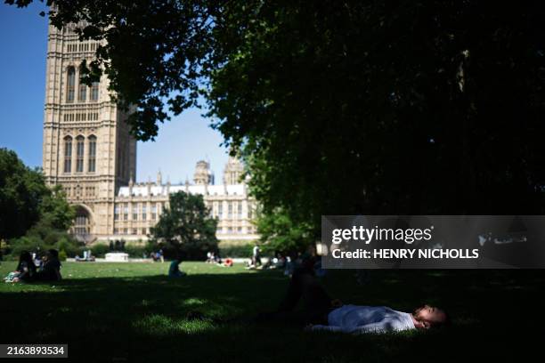 People lay on the grass in both the shade and the sunshine in Victoria Tower Gardens near the Houses of Parliament, in central London, on July 30,...