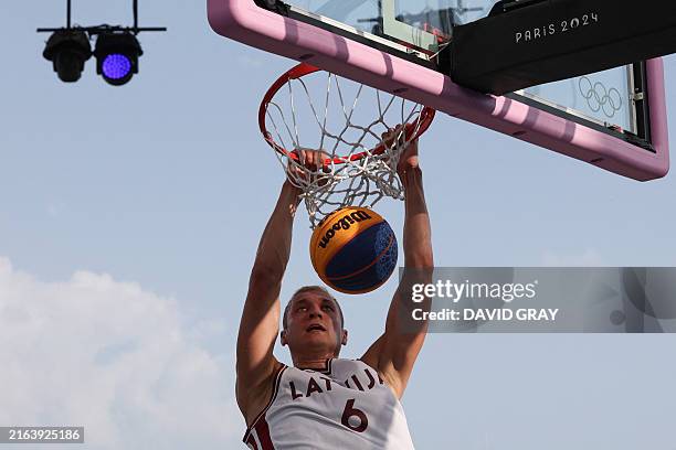 Latvia's Francis Lacis hangs onto the basket hoop in the men's pool round 3x3 basketball game between Latvia and Lithuania during the Paris 2024...