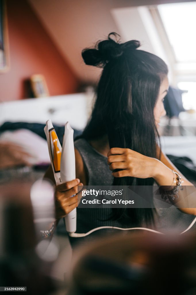 Young woman using curl tongs in vanity mirror