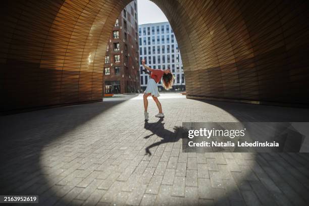 elegant slim woman with prosthetic arm dances in golden urban archway, capturing light and shadow effects - passione foto e immagini stock