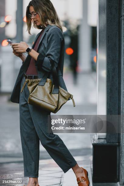 geschäftsfrau, die auf der straße der stadt sms schreibt, während sie im regen steht - slipper stock-fotos und bilder