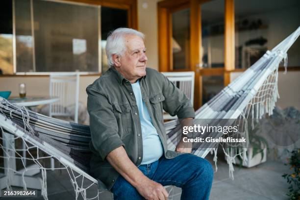 senior man sitting on a hammock and looking forward - one senior man only stock pictures, royalty-free photos & images