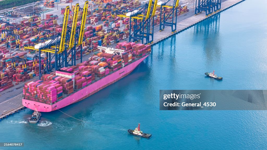 Aerial view tugboat sailing alongside container ship at container port.