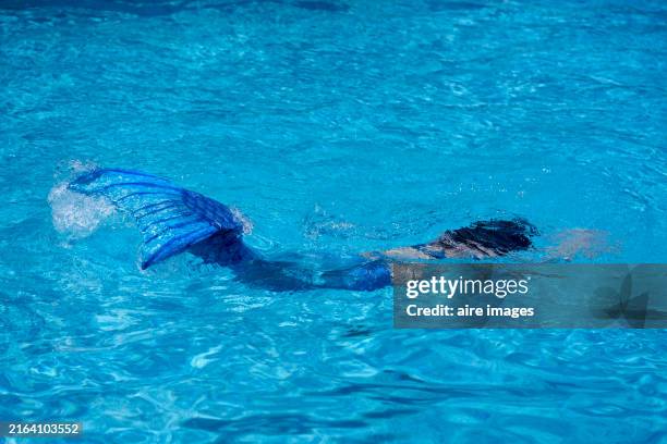 photo from behind of a caucasian girl with brown hair with aqua goggles bathing in the pool in a mermaid costume - real mermaid images stock pictures, royalty-free photos & images