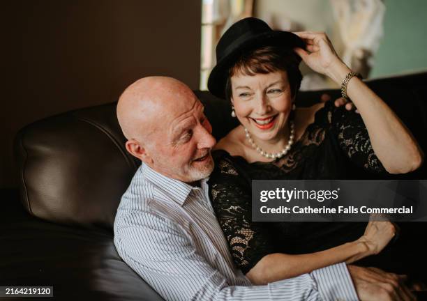 couple enjoying playful moment together while sitting on couch in cozy indoor space - woman little black dress stock pictures, royalty-free photos & images