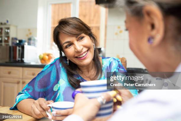 cheerful mature women having a coffee break together in a kitchen - alleen oudere vrouwen stockfoto's en -beelden