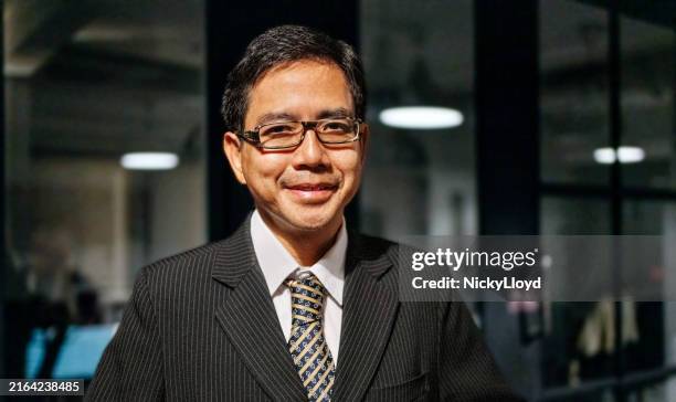 smiling asian businessman standing in office at night - low lighting stock pictures, royalty-free photos & images