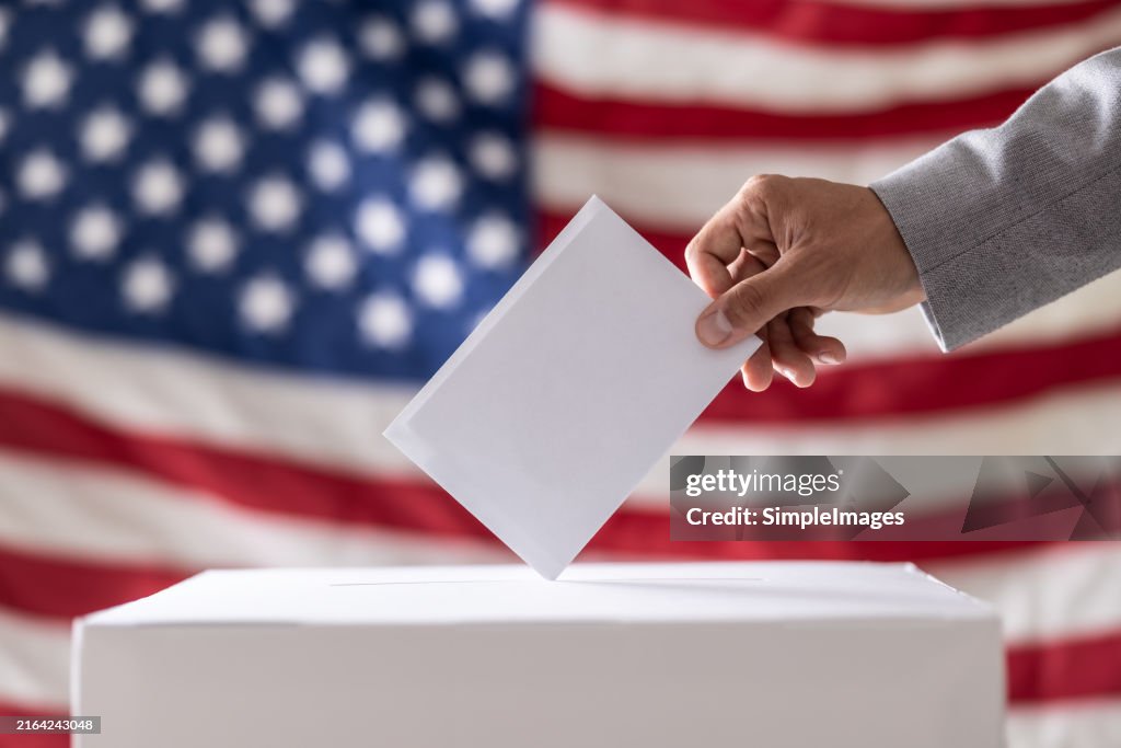 Election in USA. Man hand putting his vote into ballot box and American flag on background - Close up