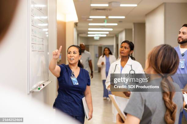 une jeune infirmière adulte fait un geste vers le tableau blanc lors d’une rencontre avec son équipe - suivi des malades photos et images de collection