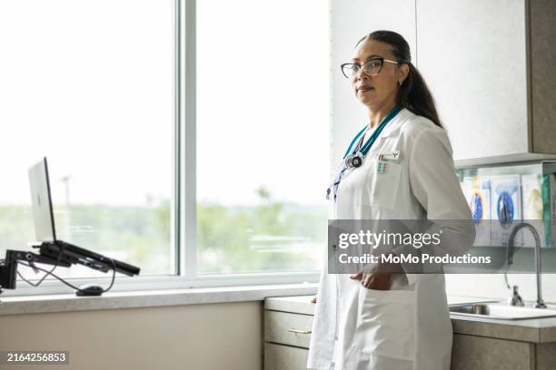 portrait of female doctor in exam room - hands in pockets stock pictures, royalty-free photos & images