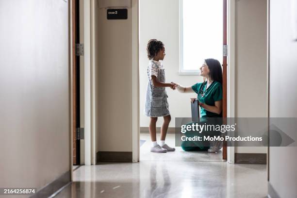 female doctor talking with young girl in doctor's office hallway - pediatric nurse stock pictures, royalty-free photos & images