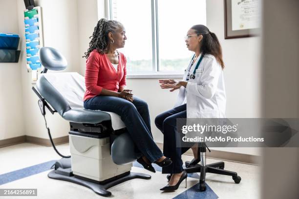 female doctor talking with senior woman in exam room - doctor stethoscope patient whole body stock pictures, royalty-free photos & images