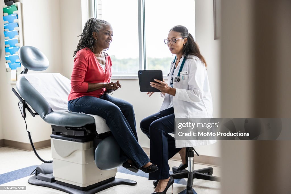 Female doctor and senior woman looking at digital tablet in exam room