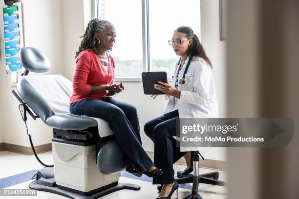female doctor and senior woman looking at digital tablet in exam room - doctor stethoscope patient whole body stock pictures, royalty-free photos & images