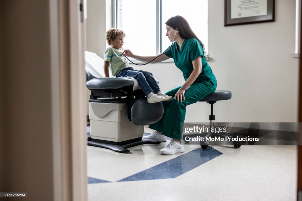Female doctor listening to young boy's heart in exam room